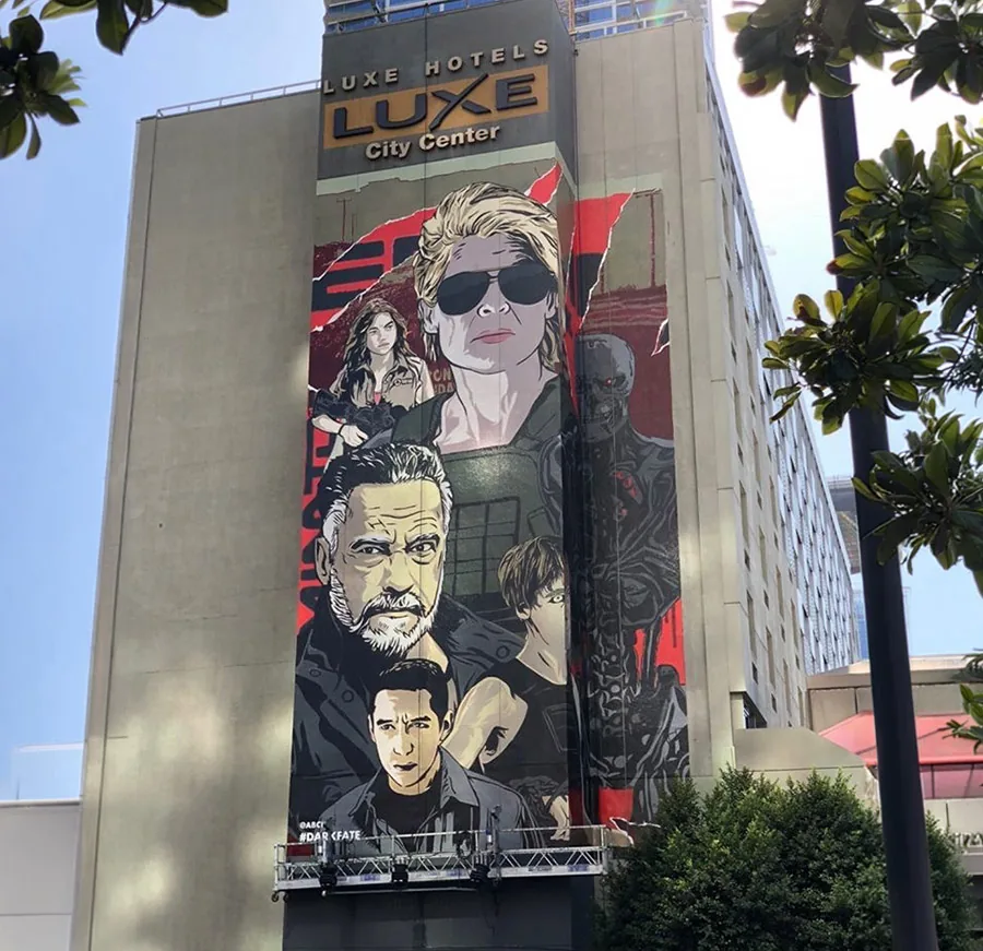 Street-level view of the Terminator: Dark Fate mural on the Luxe Hotel, framed by trees